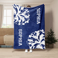 Blue cheerleading blanket held up indoors with bold white pom-pom graphics and cheer-themed lettering