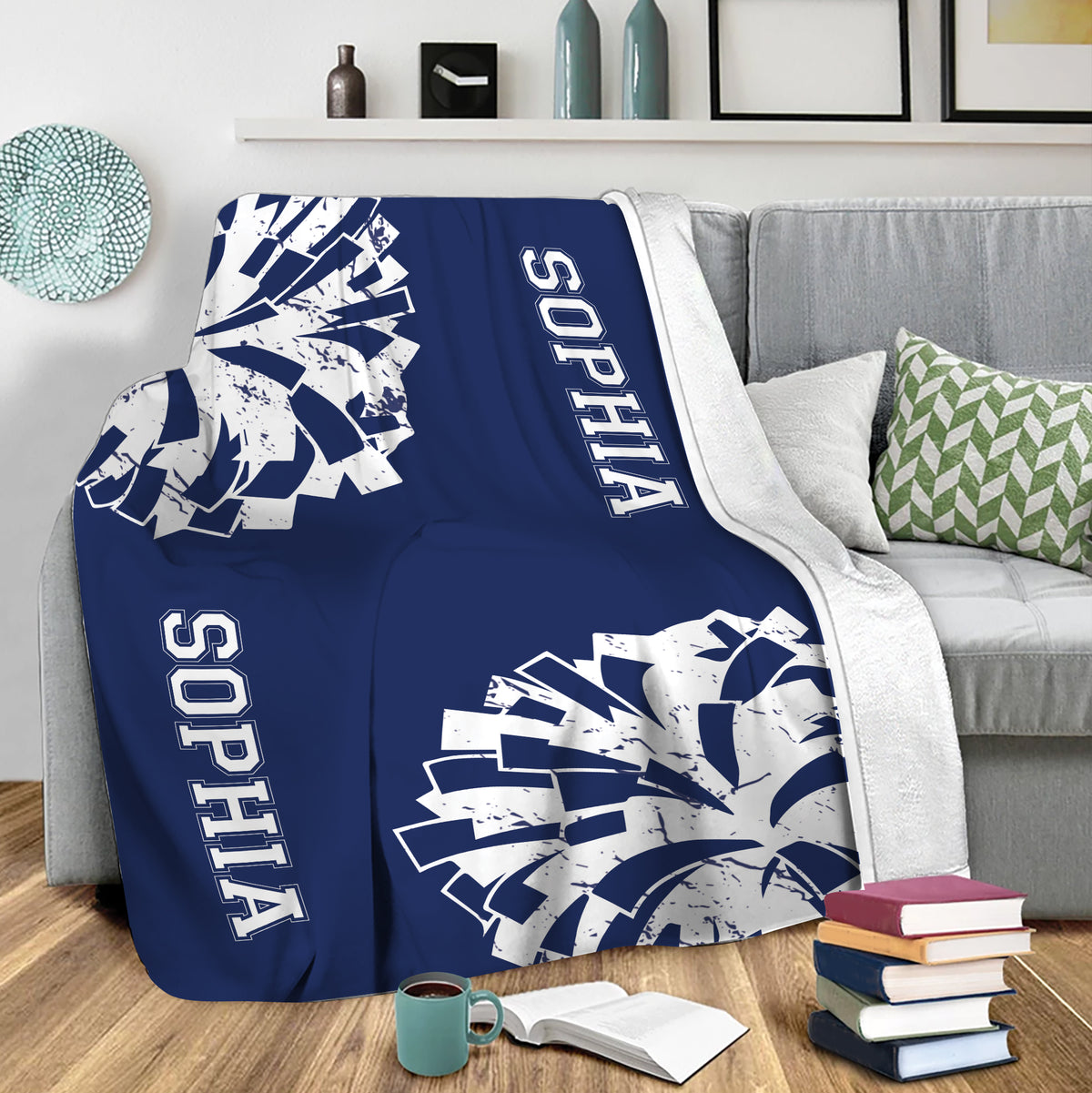 Blue cheerleading blanket draped over a sofa with bold pom-pom artwork in a living room setting