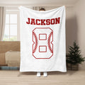 White baseball throw blanket displayed in a living room with contrasting red baseball stitching artwork