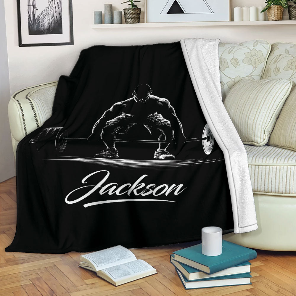 Black weightlifting throw blanket draped over a sofa with white barbell lifting artwork