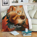 Squirrel throw blanket displayed on a sofa with an acorn and autumn woodland artwork