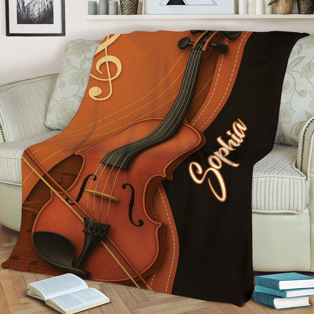 Close view of violin and bow artwork with musical notes on a warm brown throw blanket