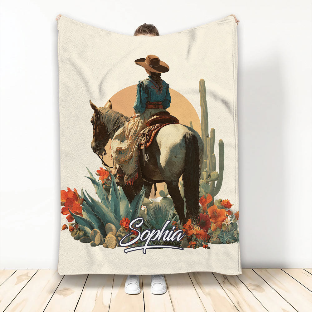 Cowgirl riding a horse through a desert scene with cacti, wildflowers, and Western artwork on a blanket
