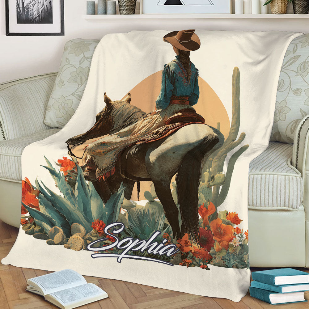 Close lifestyle view of a cowgirl on horseback surrounded by desert plants and vibrant flowers on a blanket