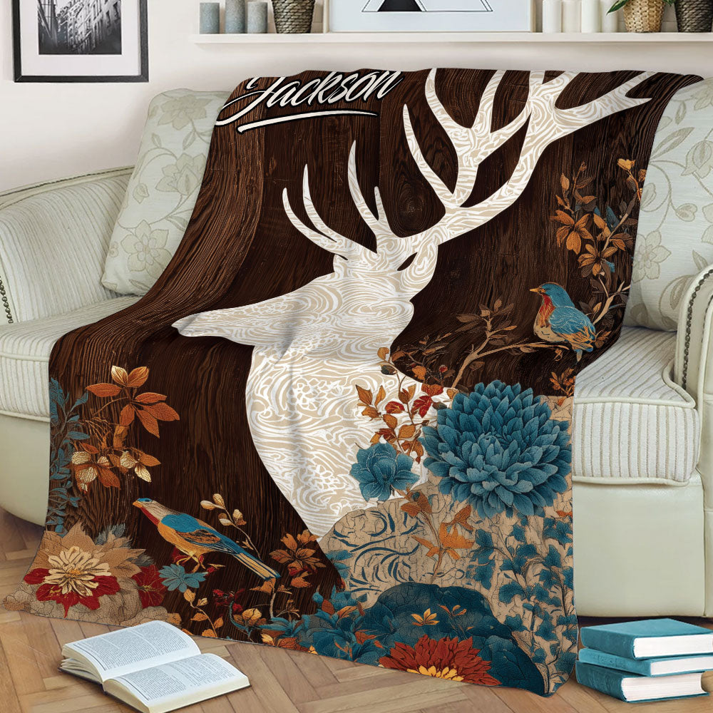 Close view of a decorative deer blanket featuring a white stag, birds, flowers, and dark woodland tones