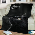 Close-up black cat throw blanket spread across a sofa with detailed fur and bright eyes