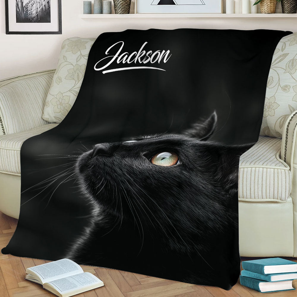 Close-up black cat throw blanket spread across a sofa with detailed fur and bright eyes