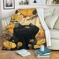 Black cat throw blanket displayed on a sofa with warm floral artwork and cozy reading decor
