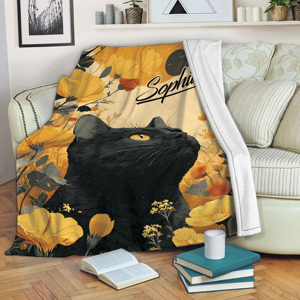 Black cat throw blanket displayed on a sofa with warm floral artwork and cozy reading decor