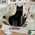 Close view of a black cat throw blanket featuring botanical foliage, stars, and moon phases