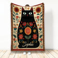 Black cat blanket with colorful floral artwork, decorative border, and folk-inspired botanical design