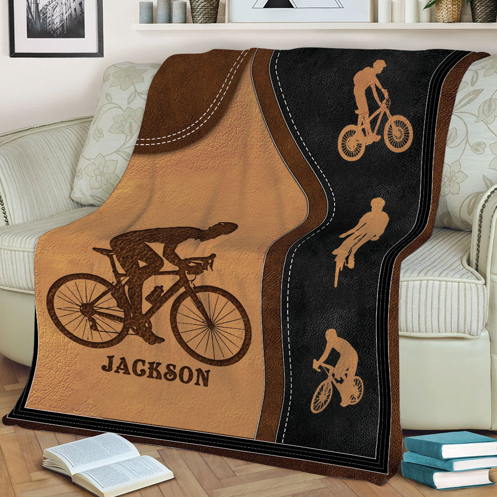 Cycling throw blanket displayed across a sofa with multiple bicycle silhouettes and bold road-style borders