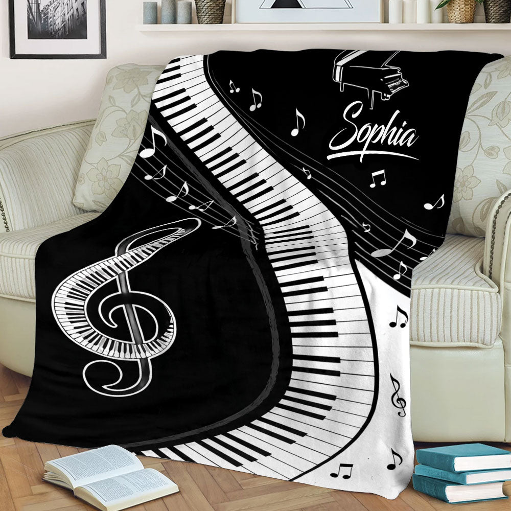 Black piano blanket displayed on a sofa with curved keyboard artwork, grand piano design, musical notes, and treble clef