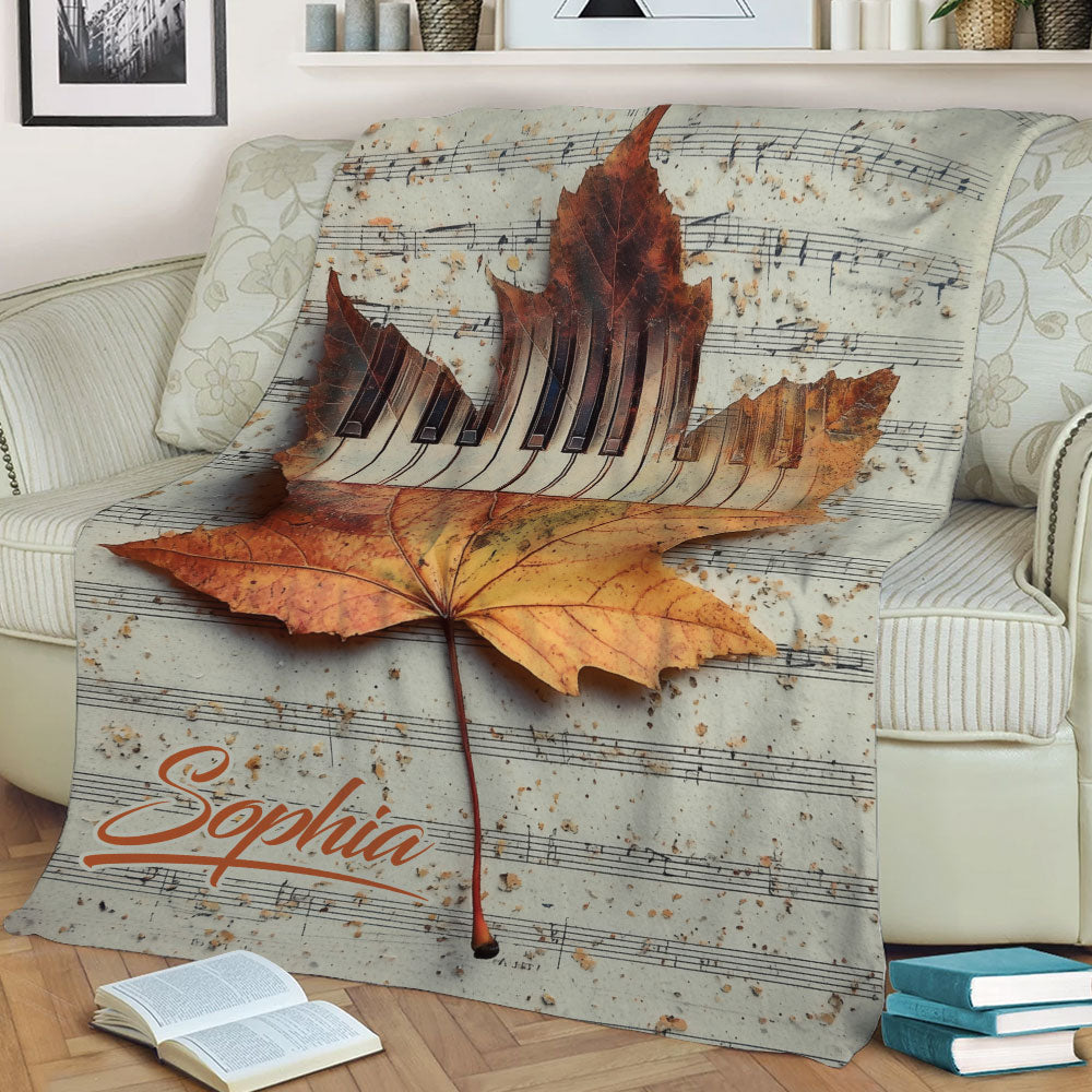 Autumn piano blanket displayed on a sofa with maple leaf artwork and musical notes