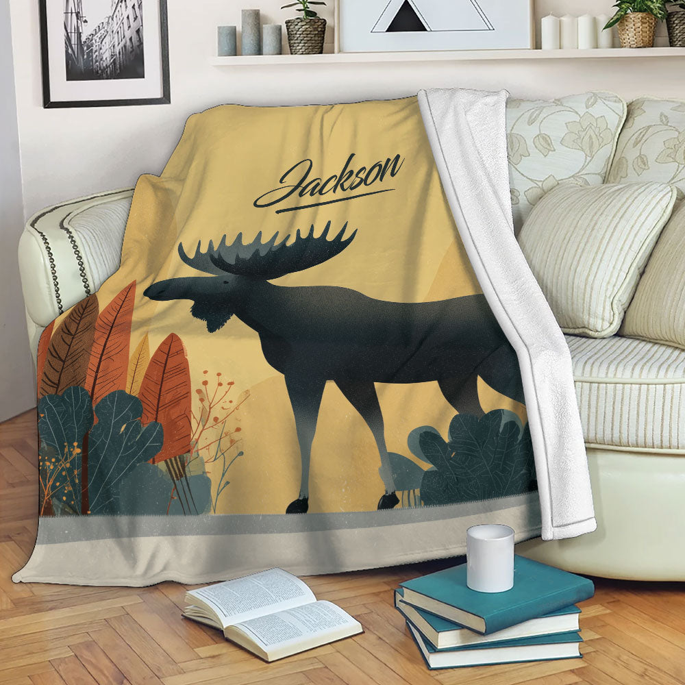 Moose blanket draped across a sofa, featuring dark wildlife artwork and autumn-inspired woodland foliage