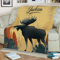 Close view of a moose throw blanket displayed on a sofa with rustic forest artwork and warm earthy colors