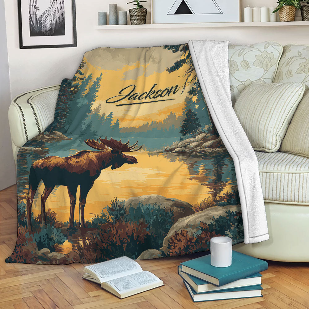 Moose blanket draped over a sofa, featuring a rustic lakeside forest scene in gold and teal tones