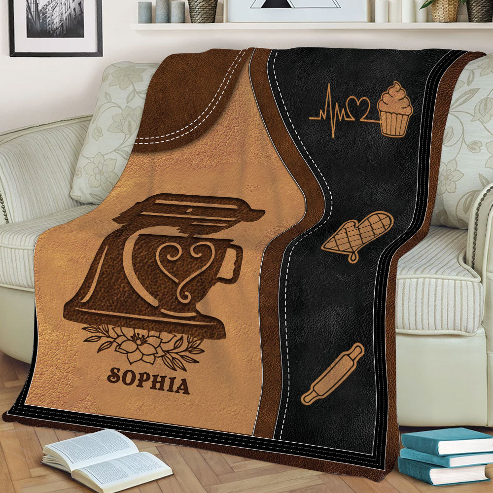 Close view of a cozy baking blanket featuring a stand mixer, cupcake, oven mitt, and rolling pin design