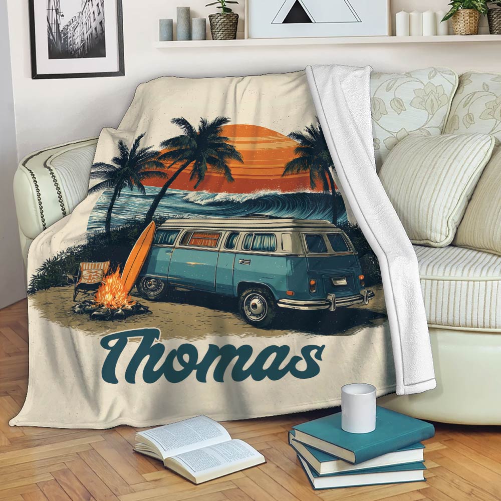 Camping blanket displayed on a sofa with a vintage camper van, beach sunset, palms, and campfire design
