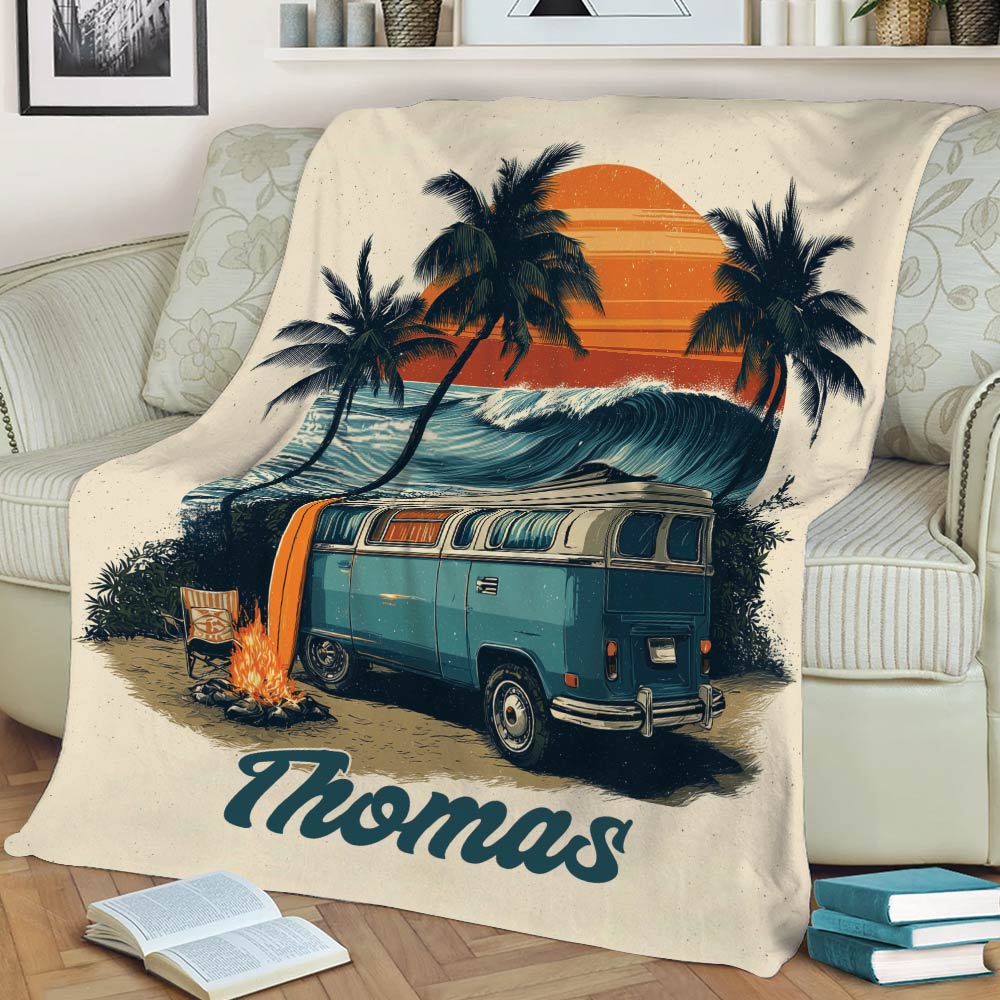 Vintage camping blanket draped over a sofa with camper van, ocean waves, palm trees, and campfire artwork