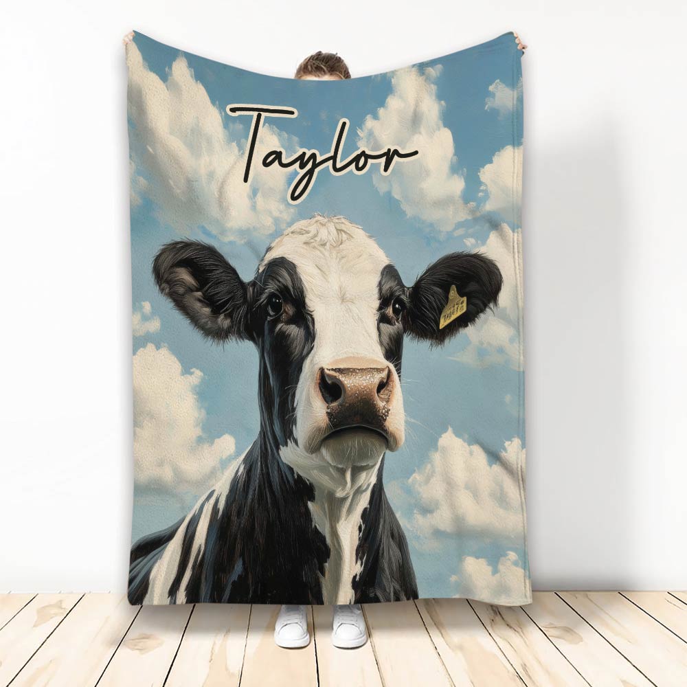 Black and white cow blanket with blue sky and cloud artwork displayed upright