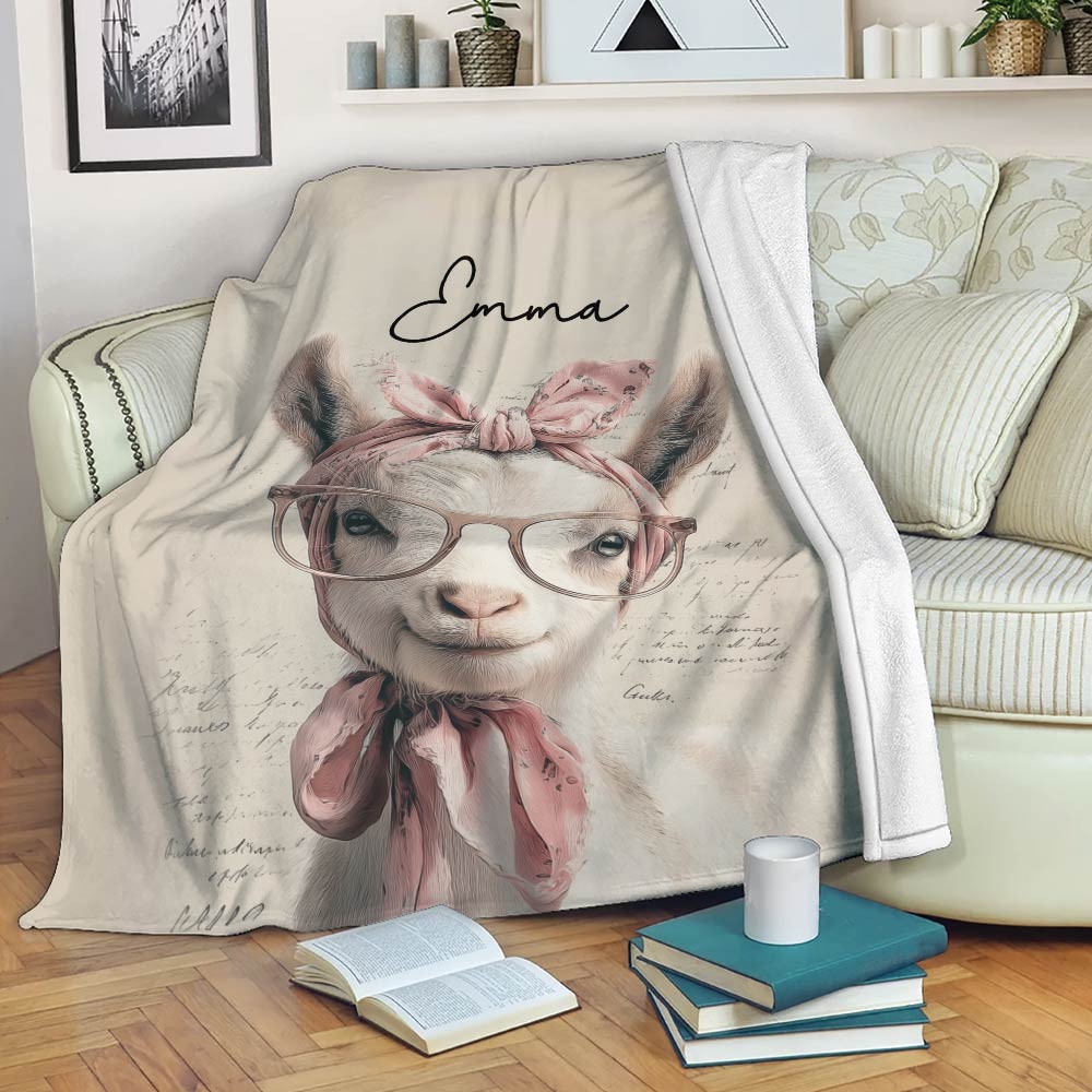 Goat throw blanket draped over a sofa, featuring whimsical glasses, pink bows, and artistic script details