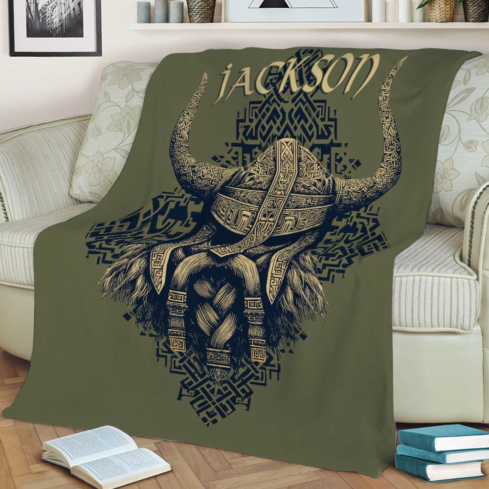 Viking throw blanket displayed on a sofa with bold horned helmet artwork in olive, navy, and gold