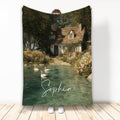 Lake house blanket featuring a storybook cottage, flower garden, clear pond, and swans in a scenic retreat design