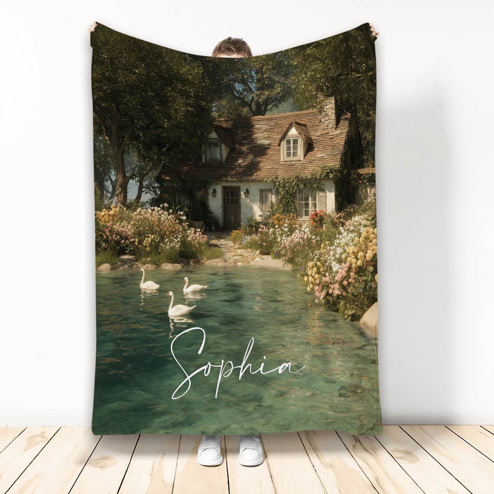 Lake house blanket featuring a storybook cottage, flower garden, clear pond, and swans in a scenic retreat design