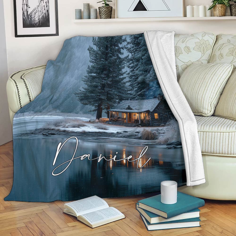 Lake house throw blanket draped over a sofa with snowy cabin and forest landscape design