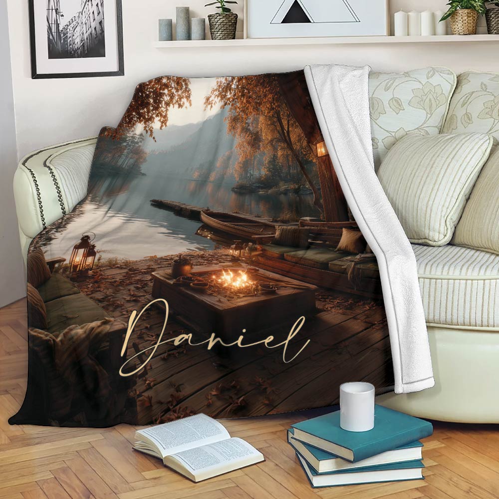 Lake House Throw Blanket draped over a sofa with autumn lake scenery, dock, boat, and warm firelight