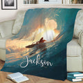Ocean surfing blanket displayed on a sofa with a silhouetted rider and painterly teal waves
