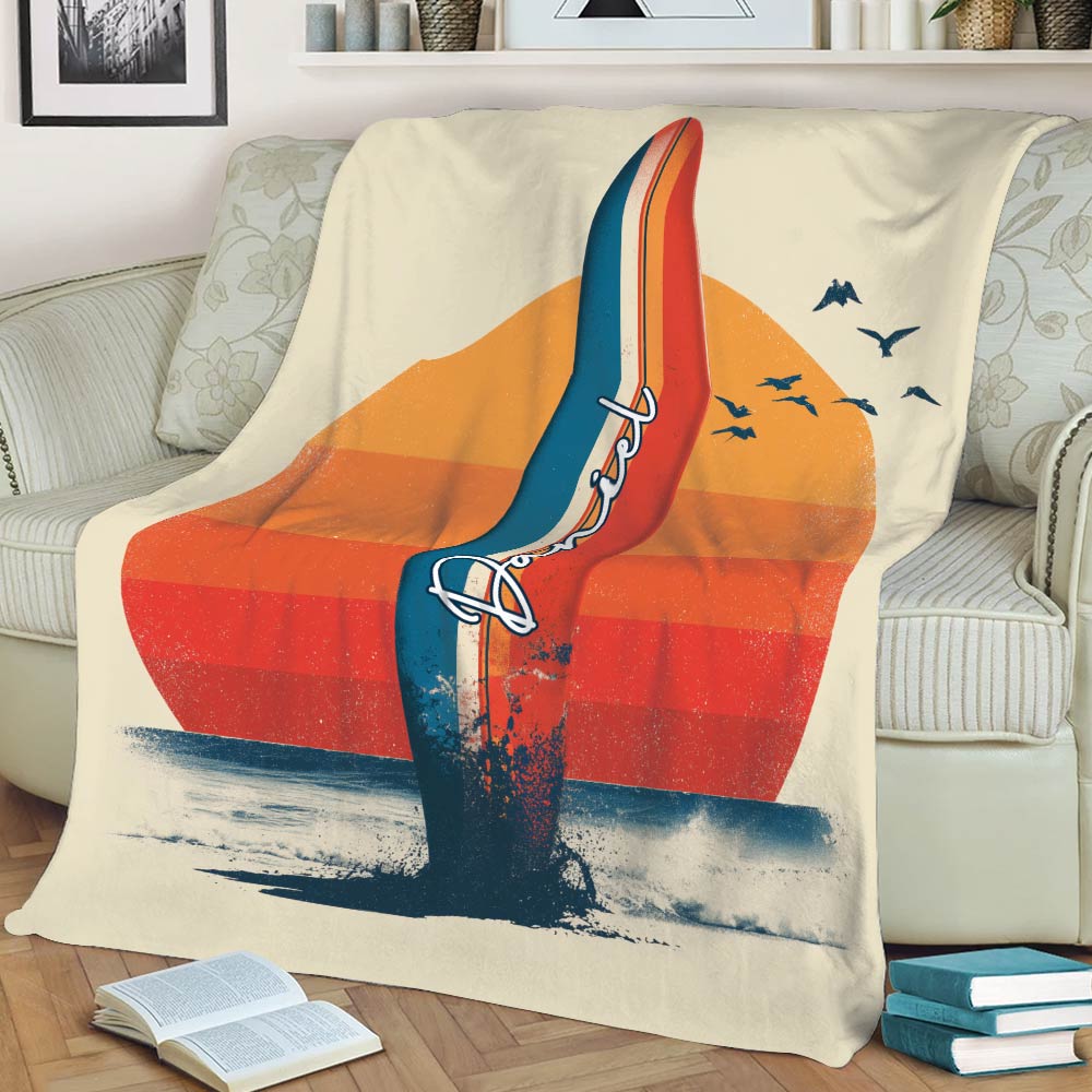 Retro surfing blanket draped over a sofa, featuring a tall surfboard, sunset, seabirds, and beach waves