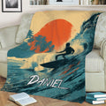 Surfing throw blanket draped over a chair, featuring a surfer, ocean wave, palms, and sunset
