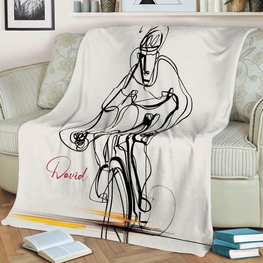 Cycling throw blanket draped over a sofa, featuring minimalist black bicycle and rider artwork