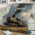 Steam train throw blanket displayed on a sofa with rustic railway artwork and a moody sky