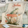 Frog throw blanket displayed on a couch with floral woodland illustration