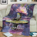 Frog throw blanket displayed on a couch with a large pink water lily, lily pad, and colorful pond artwork