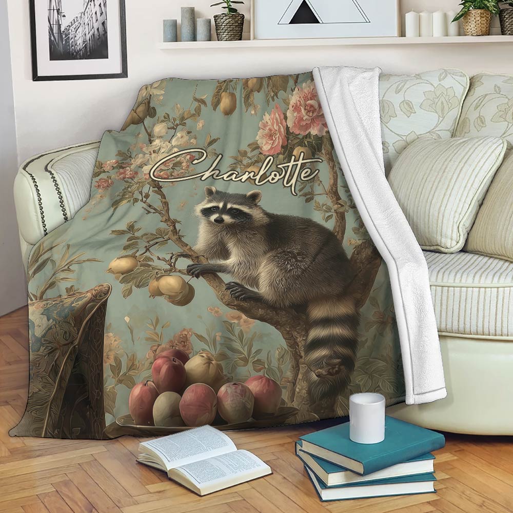 Raccoon throw blanket with botanical artwork draped over a sofa beside books