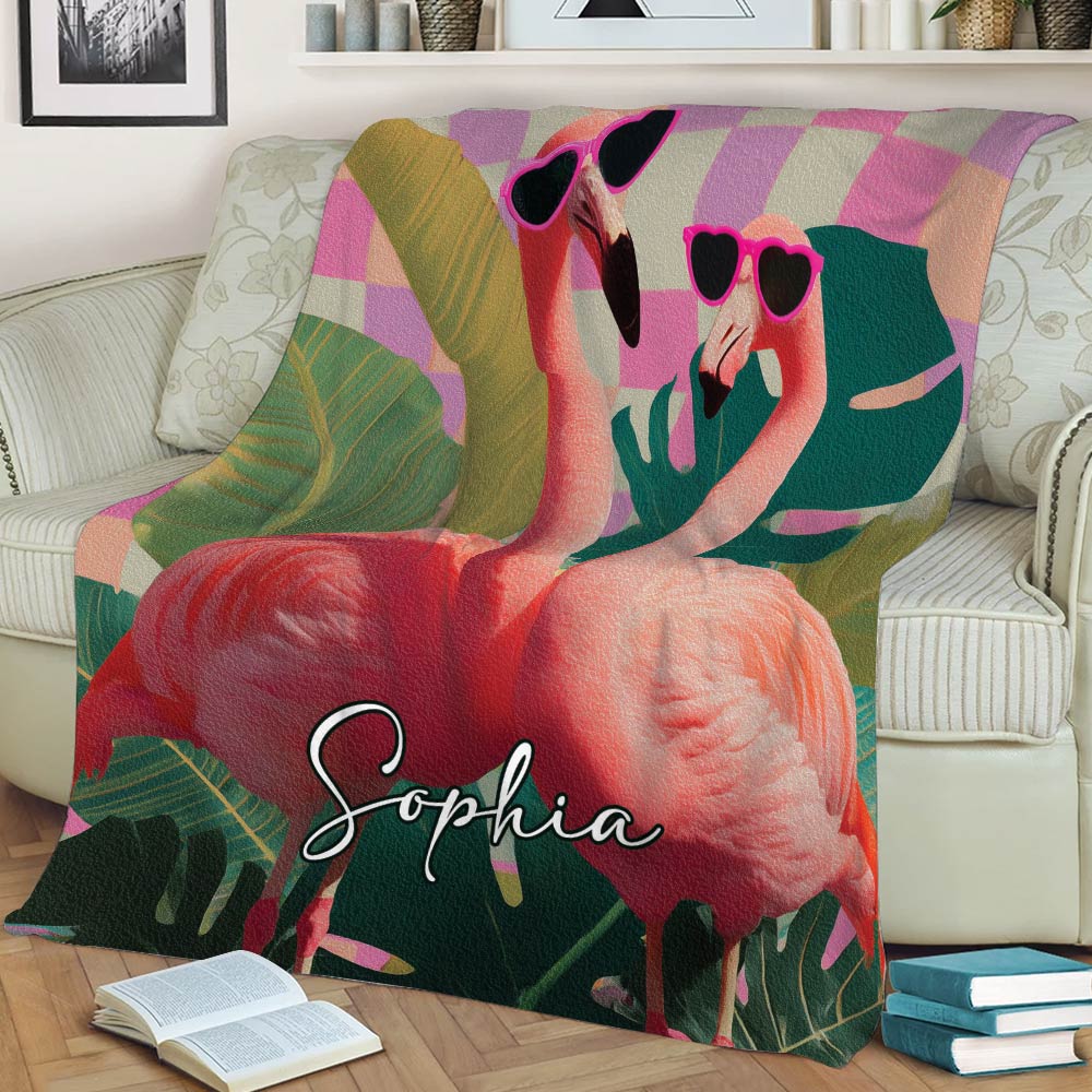 Close view of a colorful flamingo blanket draped over a sofa with tropical leaves and playful sunglasses