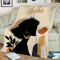 Living room display of an African-inspired blanket with Black woman silhouette, botanical details, and neutral tones
