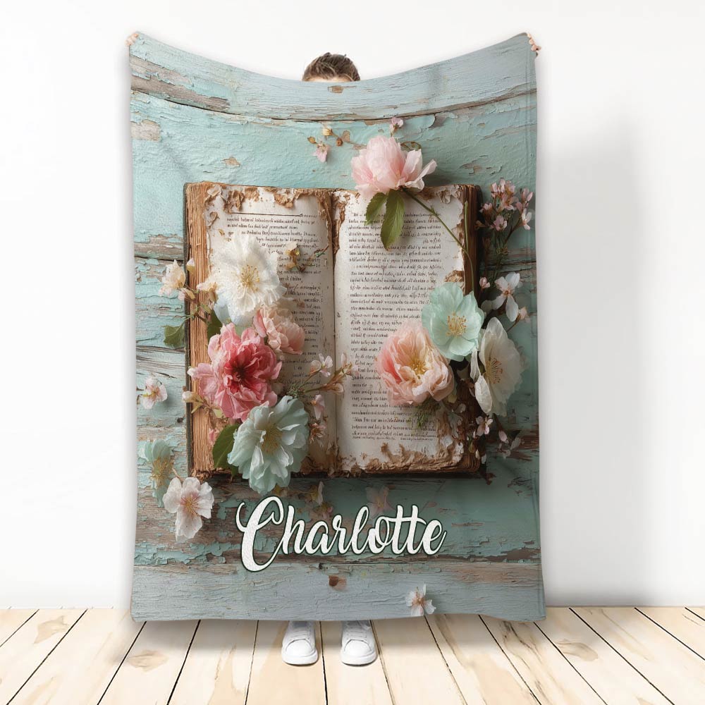 Floral open book artwork on a cozy blanket displayed against a rustic blue wood background