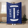 Blue football throw blanket held up indoors with a large white football and laces design