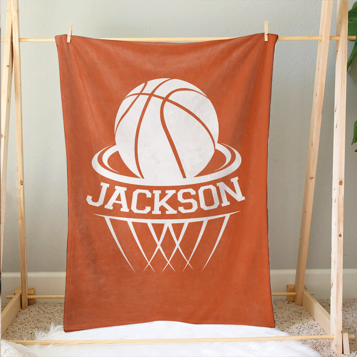 Orange basketball blanket hanging on a wooden frame with bold white hoop artwork