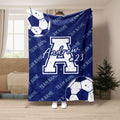 Blue soccer throw blanket held up indoors with large soccer ball graphics and bold team-inspired artwork