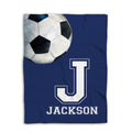 Flat-lay soccer blanket showing an oversized soccer ball and bold athletic letter on a navy background