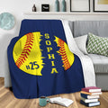 Softball throw blanket draped over a sofa with bold yellow, red, and navy sports artwork