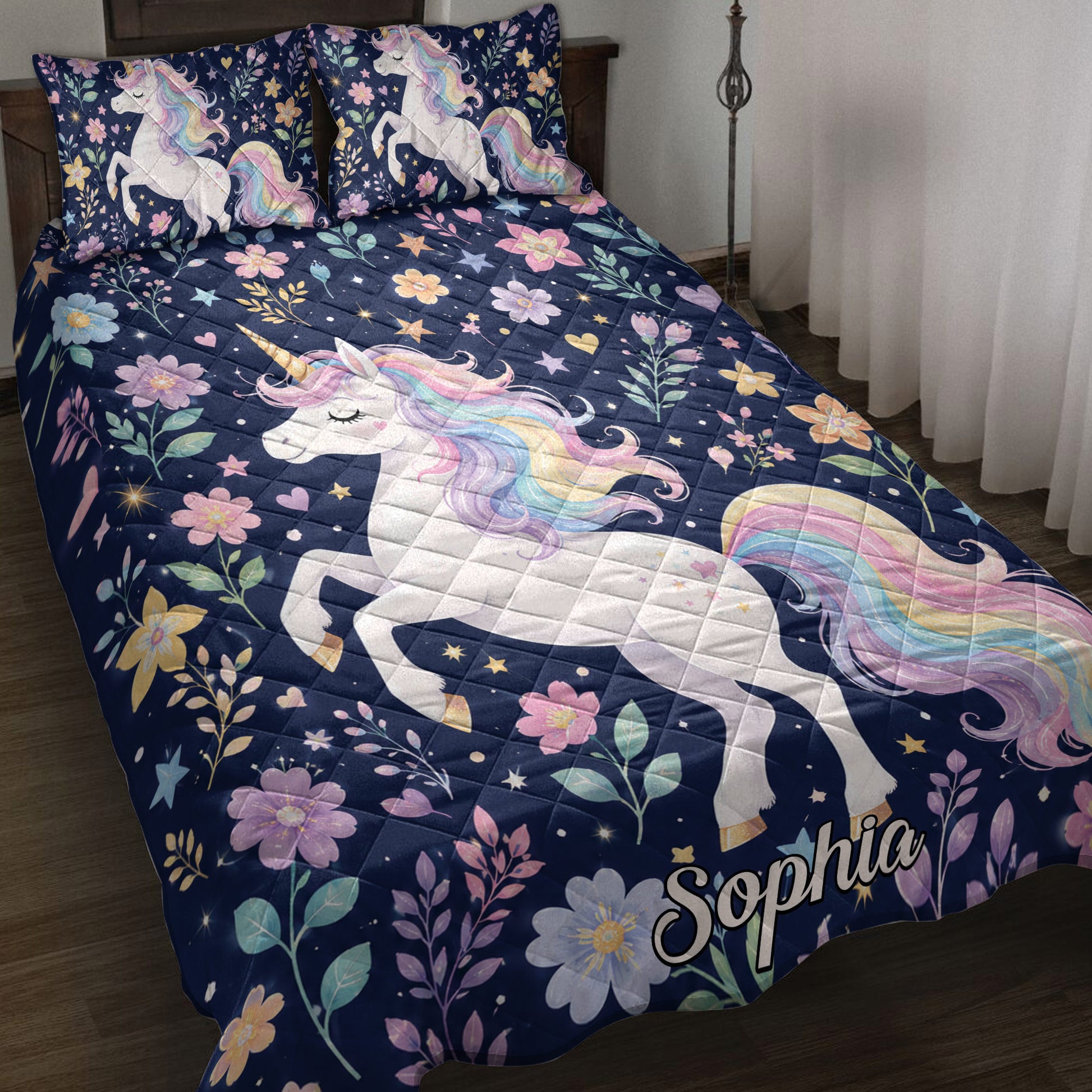 Unicorn quilt blanket displayed on a bed with pastel rainbow manes, flowers, stars, and navy floral artwork