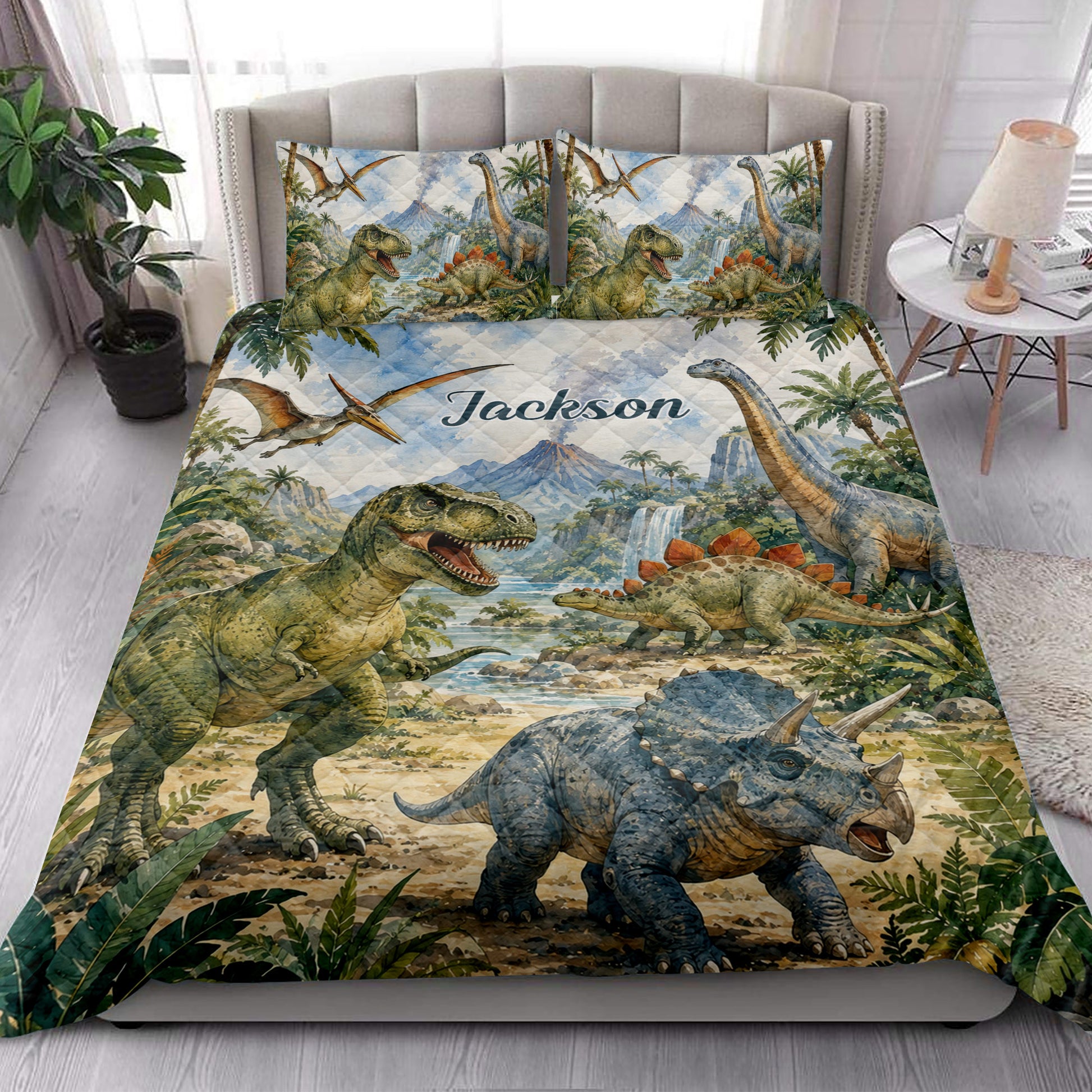 Dinosaur quilt blanket styled on a bedroom bed with T-rex, sauropod, triceratops, jungle plants, and waterfalls