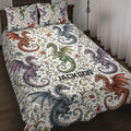 Dragon quilt blanket spread across a bed with colorful winged dragons, flowers, stars, and moon artwork